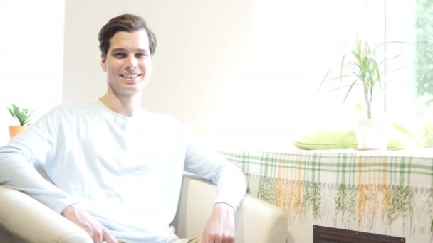 Close up portrait of a cheerful young man sitting on modern sofa — Stock Video