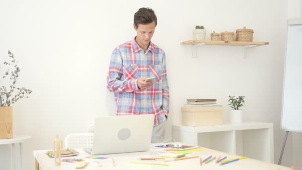 Diseñador hombre utilizando el teléfono inteligente en la oficina creatve enviar un mensaje en las redes sociales — Vídeos de Stock