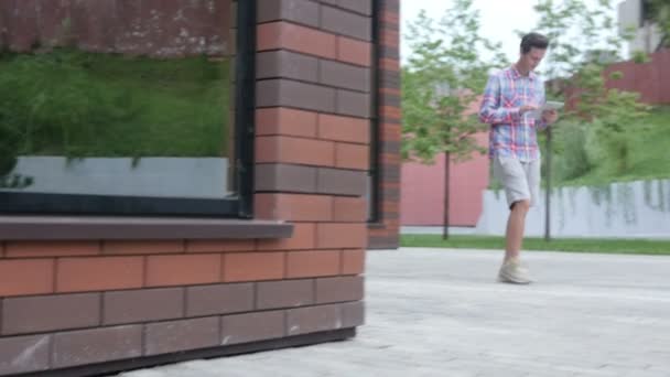 Случайный молодой ходячий человек с помощью планшетного компьютера — стоковое видео