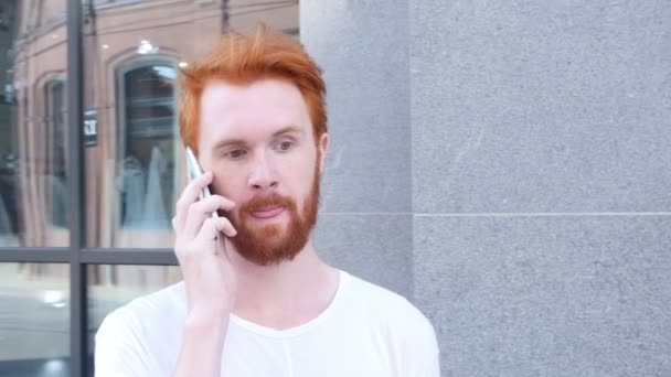 Hablando por teléfono, w / cámara moviéndose alrededor del hombre joven, al aire libre, Cabellos rojos — Vídeo de stock