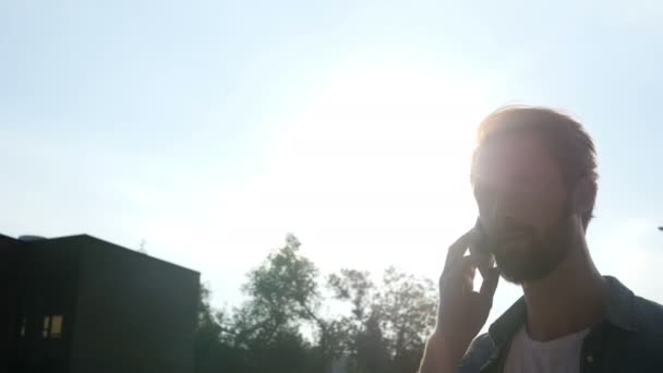 Caminhando e conversando ao telefone durante o pôr do sol, em frente ao sol — Vídeo de Stock