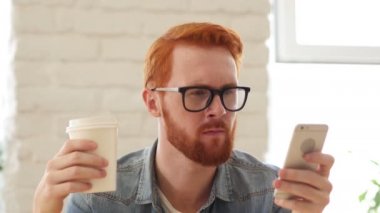 Adam sakal ve kırmızı kılları kullanma Smartphone, telefon ve içme kahve, çay