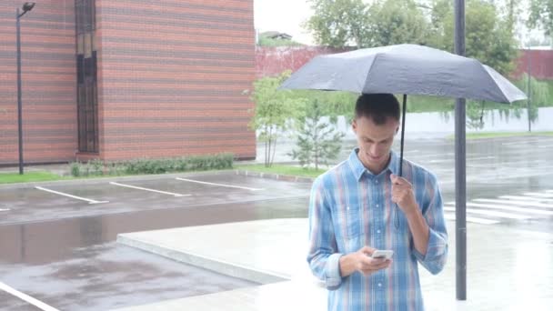 Utilizzando Smartphone, in piedi sotto l'ombrello durante la pioggia — Video Stock