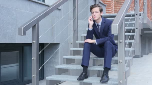 Office dışındaki merdivenlerde oturan genç işadamı telefon konuşma, müzakere, — Stok video