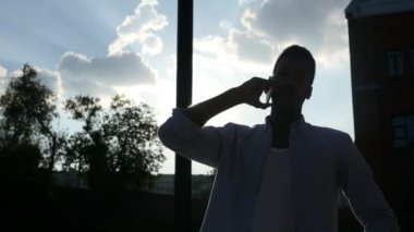 Telefon, günbatımı sırasında güneş önünde konuşan siluet siyah adam