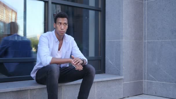 Ao ar livre esperando, assistindo o tempo, sentado jovem preto bonito homem — Vídeo de Stock
