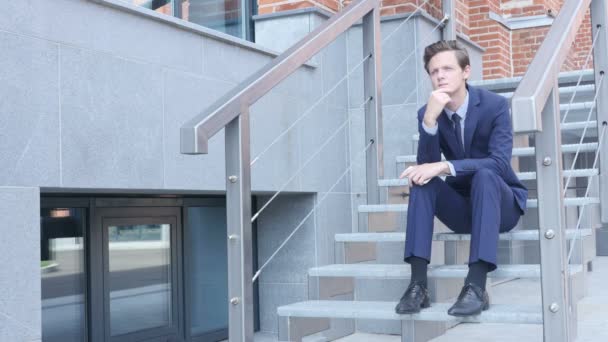 Zamyślony myślenia młody biznesmen siedząc na schodach spoza biura — Wideo stockowe