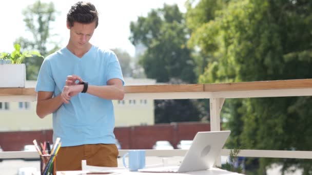 Sonniger Tag, Mann steht und benutzt Smartwatch auf Balkon, Gadget — Stockvideo