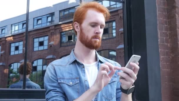 Homem usando Smartphone, ao ar livre, cabelos vermelhos e barba — Vídeo de Stock