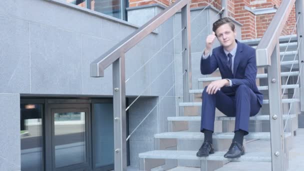 Daumen hoch von jungem Geschäftsmann, der auf Treppe vor Büro sitzt — Stockvideo