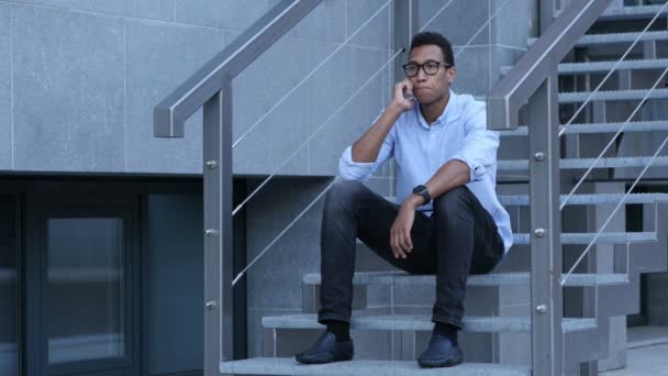 Jeune homme noir assis sur les escaliers et parlant au téléphone — Video