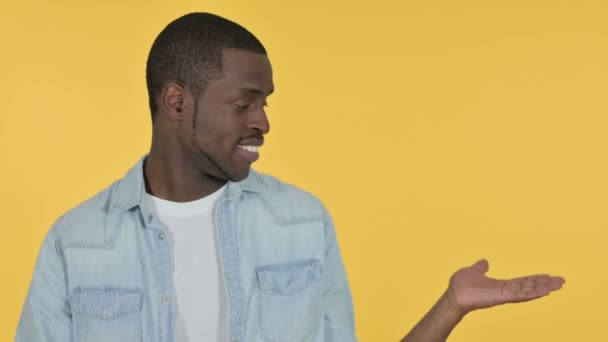 Ung afrikansk man håller produkt på handflatan, gul bakgrund — Stockvideo