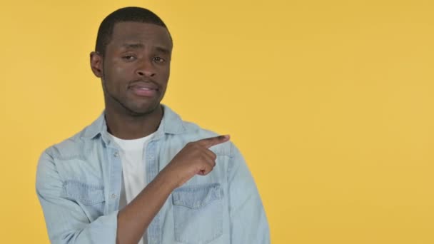 Hombre joven africano señalando el producto, fondo amarillo — Vídeos de Stock