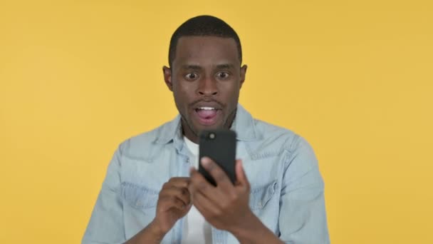 Jovem homem africano comemorando no smartphone, fundo amarelo — Vídeo de Stock