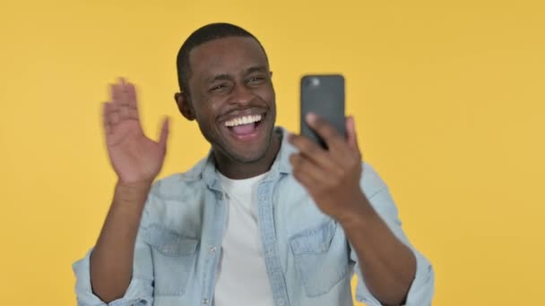 Hombre joven africano hablando para el chat de vídeo a través de Smartphone, fondo amarillo — Vídeo de stock