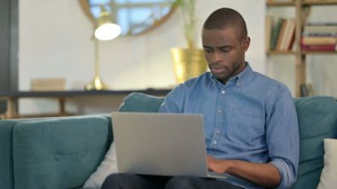 Dizüstü bilgisayarlı genç Afrikalı Adam Koltukta Düşünüyor 
