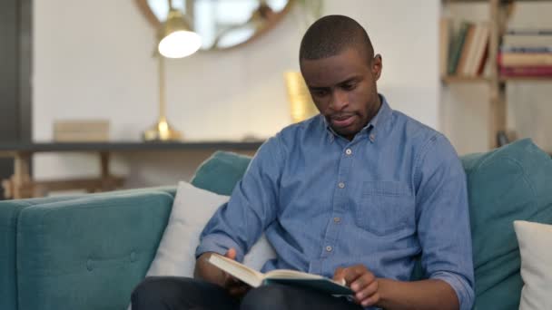 Young African Man Reading Book on Sofa — Stok Video