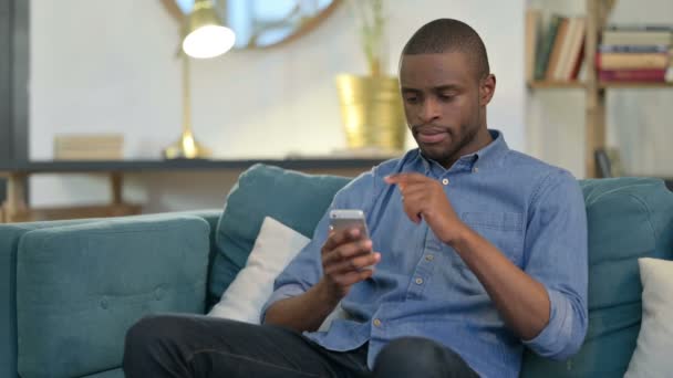 Joven africano serio usando Smartphone en el sofá — Vídeos de Stock