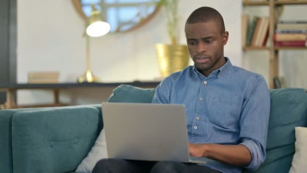 Jonge Afrikaanse man met laptop met polspijn op de bank — Stockvideo