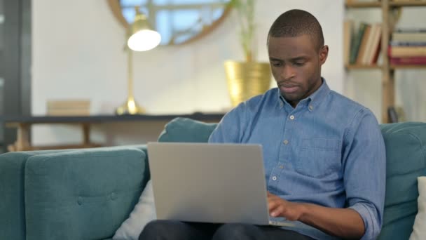 Mooie jonge Afrikaanse man met behulp van laptop op de bank — Stockvideo