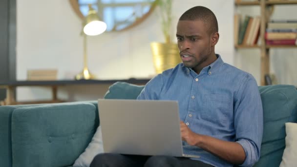 Hombre joven africano con portátil reaccionando al fracaso en el sofá — Vídeos de Stock
