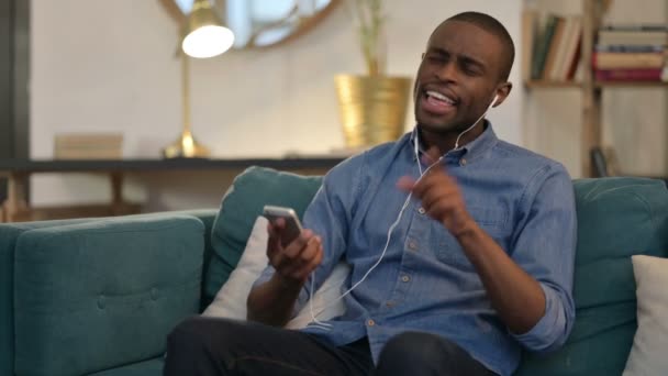 Joven africano escuchando música en el Smartphone en el sofá — Vídeos de Stock