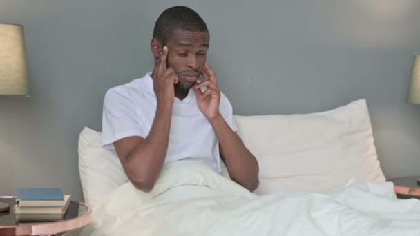 Młody Afrykanin z bólem głowy siedzi w łóżku — Wideo stockowe
