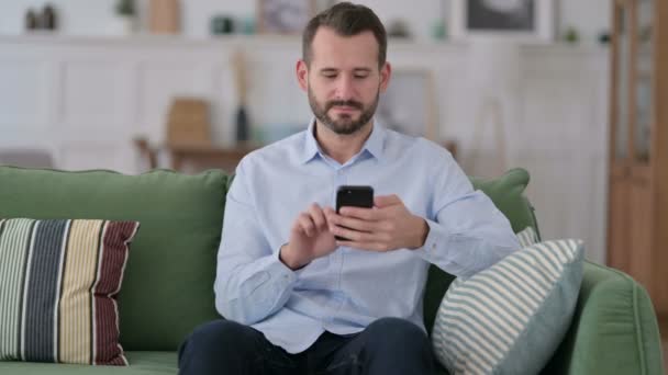Joven serio usando Smartphone en el sofá — Vídeos de Stock