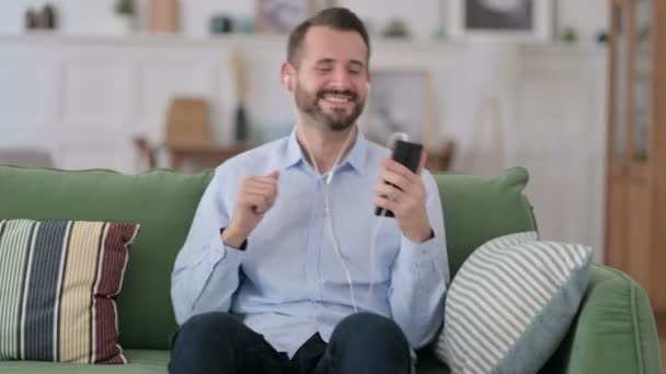 Hombre joven escuchando música en el Smartphone en casa — Vídeos de Stock