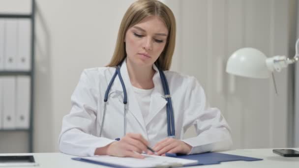 Ung kvinnlig doktor som skriver på papper på jobbet — Stockvideo