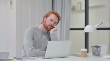 Laptop 'u olan kızıl saçlı adam iş yerinde kestiriyor. 