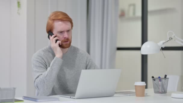 Dühös vörös férfi laptoppal beszél okostelefonon — Stock videók