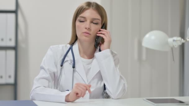 Молода жінка лікар розмовляє на смартфоні на роботі — стокове відео