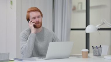 Dizüstü bilgisayarlı kızıl saçlı adam Smartphone 'da konuşuyor. 
