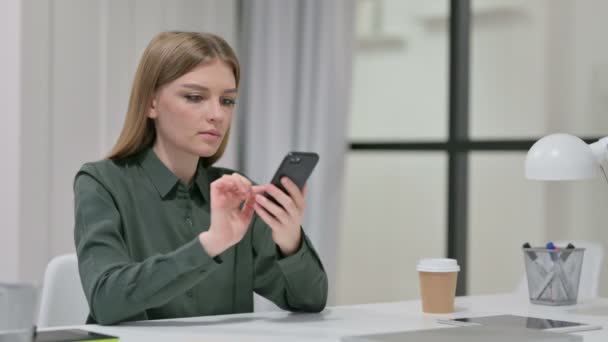 Приваблива молода жінка використовує смартфон на роботі — стокове відео