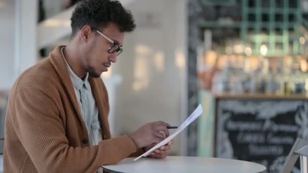 Hombre africano escribiendo en papel en café — Vídeos de Stock