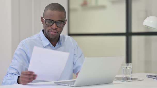 Hombre africano leyendo documentos y trabajando en el ordenador portátil — Vídeo de stock