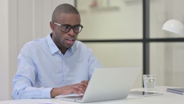 Успешный африканский человек празднует на ноутбуке на работе — стоковое видео