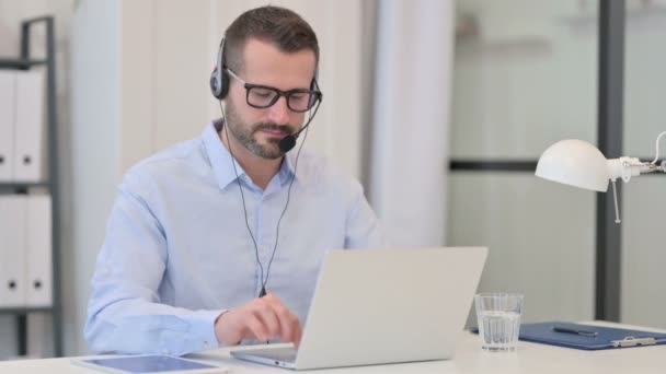 Middeleeuwse man met headset glimlachend naar de camera tijdens het gebruik van laptop — Stockvideo