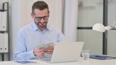 Bilgisayarda çalışırken Orta Yaşlı Adam Dolar Sayıyor 