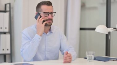 Orta yaşlı adam iş yerinde akıllı telefondan konuşuyor. 