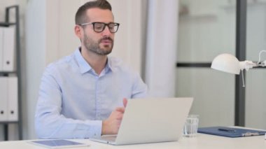 Orta yaşlı adam iş yerindeki laptopta video görüşmesi yapıyor. 