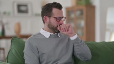 Orta yaşlı adam koltukta otururken öksürüyor. 