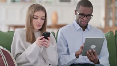 Kadın akıllı telefonu kullanırken, erkek evde tablet kullanıyor, çift 