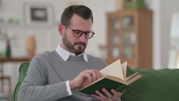 Medelålders man Läsa bok medan du sitter på soffan — Stockvideo