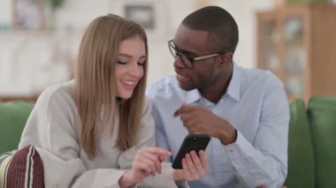 Mutlu Karışık Irk Çifti evde akıllı telefon kullanıyor. 
