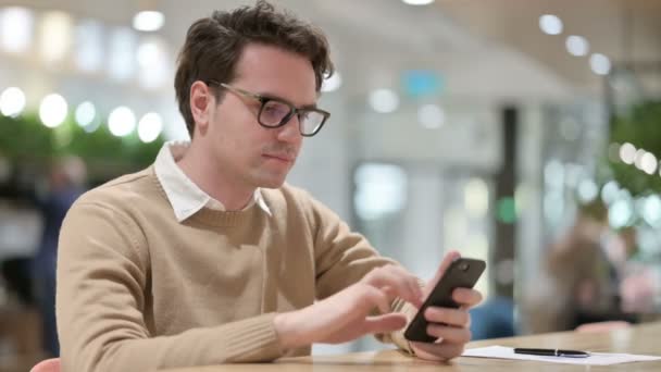 Designer masculino jovem perturbado com perda no smartphone, no escritório — Vídeo de Stock