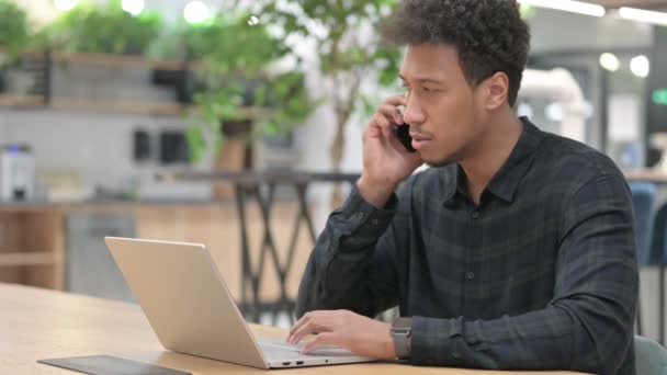 Afrikansk amerikansk man med bärbar dator talar på smartphone — Stockvideo
