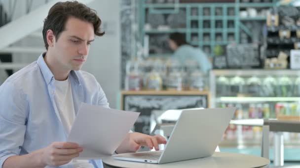 Молодой человек с документами для чтения ноутбуков в кафе — стоковое видео