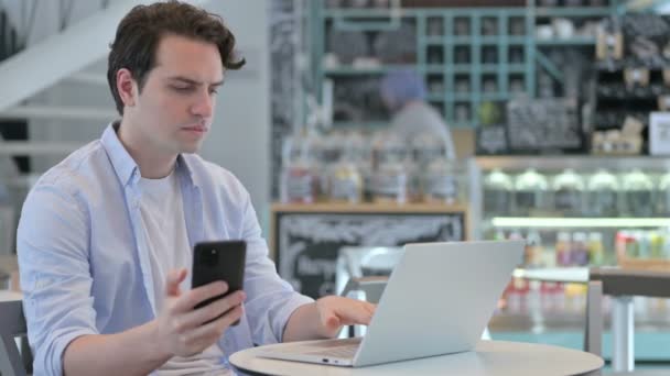 Fiatal férfi Laptop segítségével Smartphone a Cafe — Stock videók